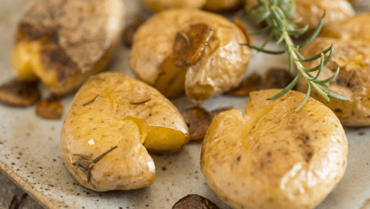 Smashed potatoes with rosemary on a plate.