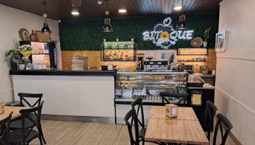 Cozy café interior with a counter, pastries on display, and a neon 'Boutique' sign on the wall.