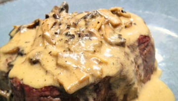 Steak with creamy mushroom sauce on a blue plate.