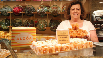 Woman holding pastries behind a counter with candy jars and a cake box.