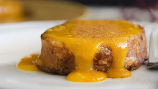 Small dessert with yellow sauce on a white plate, fork on the side.