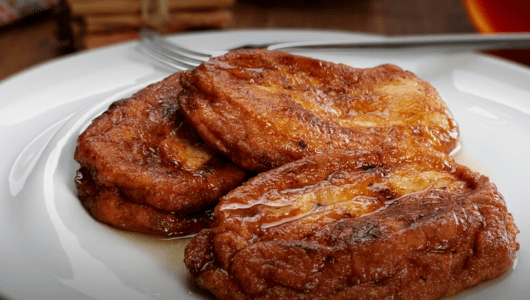 Three syrup-covered French toast slices on a white plate with a fork.