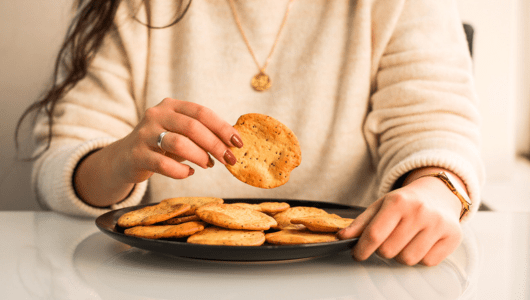 Person holding a cracker from a plate of assorted crackers on a table.