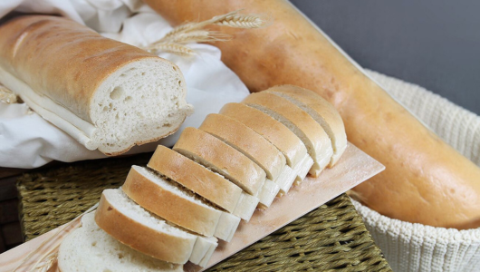 Sliced and whole loaves of bread on a woven surface with wheat decorations.