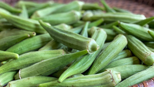 Close-up of a pile of fresh green okra on a woven surface.