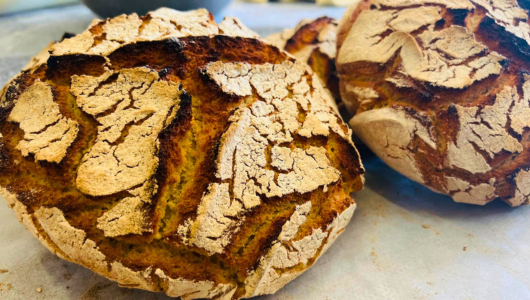 Two round loaves of rustic, crusty Portuguese corn bread with cracked surfaces.