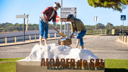 The story of salt in Portugal - Statue of two people collecting salt in Alcácer do Sal, Portugal with a road sign in the background.