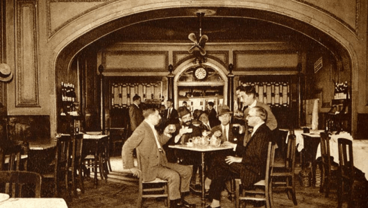 Vintage photo of men in suits at a café table in an ornate room with a large arch.