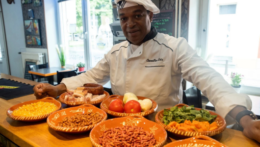 Chef in uniform presents various ingredients in colorful dishes on a counter.