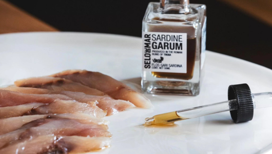 Sliced fish on plate with jar labeled 'Sardine Garum' and eyedropper.