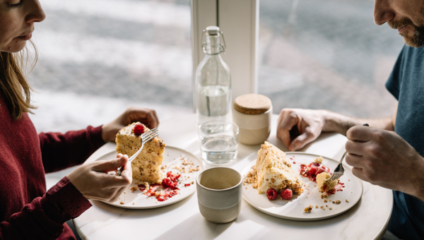 Two people eating dessert with raspberries at a small round table.
