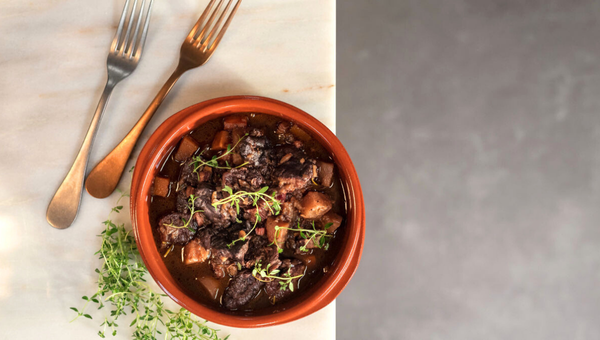 Beef stew with herbs in a bowl next to two forks on a marble surface.