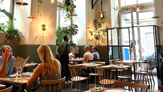 Modern cafe interior with wooden furniture, plants, and people dining.