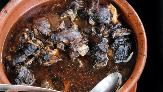 Clay pot with dark meat stew and a silver spoon on the side.