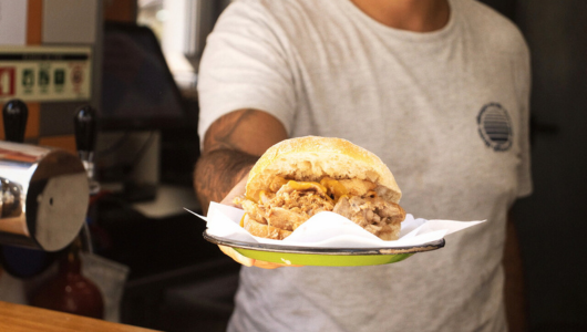 Person in a t-shirt holding a sandwich on a plate with a napkin.