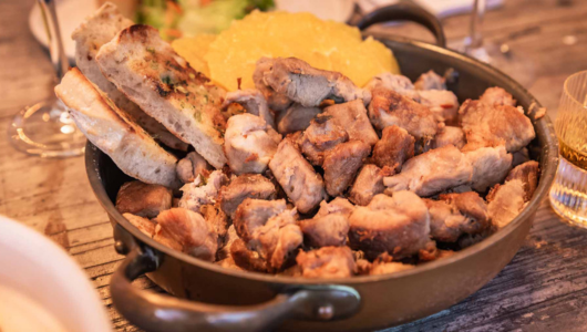 Cooked meat pieces with bread and garnish in a pan on a wooden table.