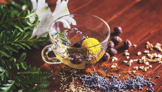 Glass cup of herbal tea with flowers and loose herbs on a wooden table.