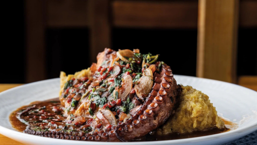 Grilled octopus with herbs served on mashed potatoes on a white plate.