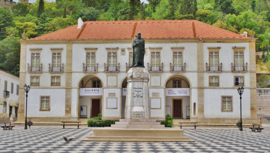 Statue in front of a historic building with arches and a checkered plaza.