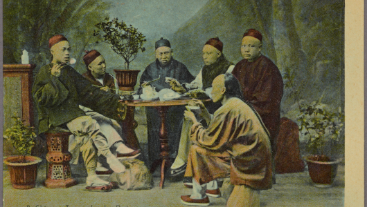 Group of people in traditional attire sitting around a table, holding pipes and cups.