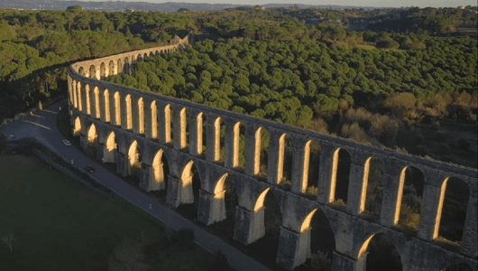 Aerial view of a long stone aqueduct stretching through a forested landscape.