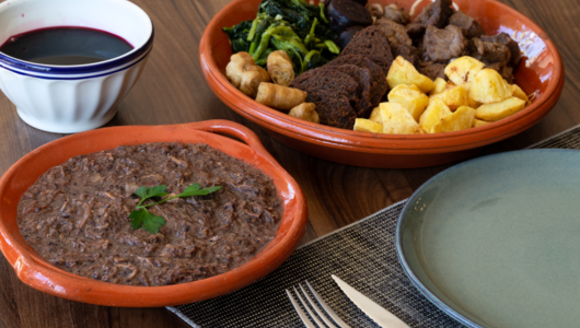 Dishes with meat, potatoes, greens, and a brown sauce on a wooden table set for a meal.