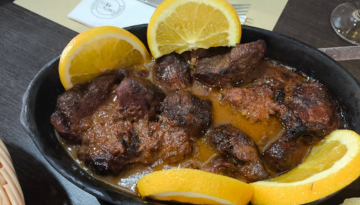 Stew with meat and orange slices in a black dish on a table.