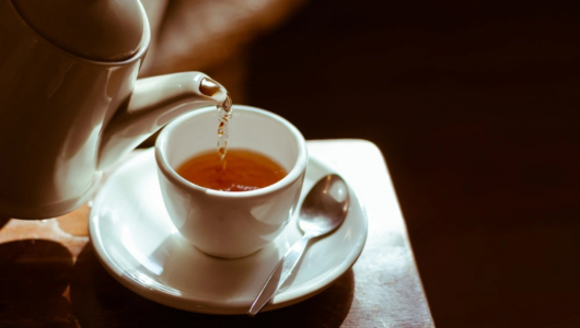 Tea being poured into a white cup with a spoon on a saucer.