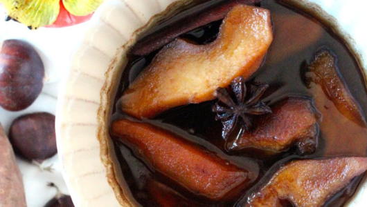 Poached pear slices in dark syrup with star anise in a bowl.