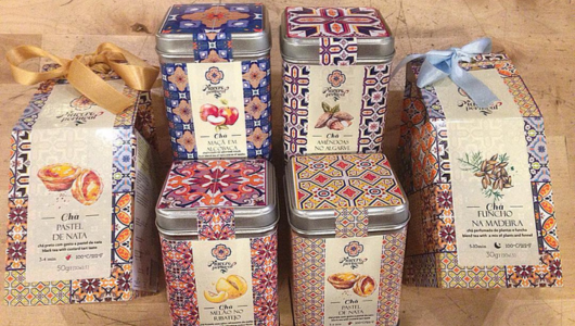 Colorful tea tins with ornate patterns, ribbons, and Portuguese labels on a wooden surface.