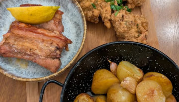 Dishes with roasted potatoes, crispy bacon with lemon, and fried chicken on a wooden table.