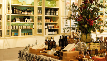 Shop interior with shelves of jars and bottles, and a table with various items and a floral arrangement.