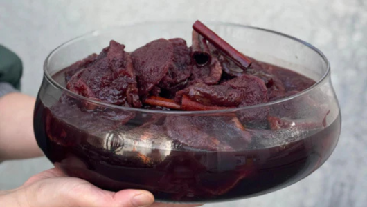Hands holding a bowl of maroon stew with chunks and cinnamon sticks.