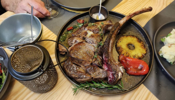 Large grilled steak with pineapple and red pepper on a plate, served with sauce and herbs.