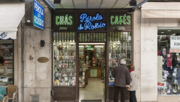 Couple standing outside a tea and coffee shop with neon signs in a city street.