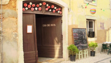 Entrance of Casa das Ratas with decorative flowers and a menu board outside.