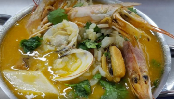 Close-up of seafood soup with prawns, clams, and herbs in a bowl.