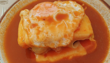 Egg-topped sandwich covered in sauce on a plate.