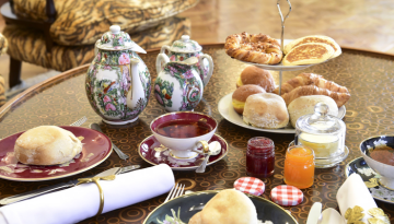 Elegant breakfast table with pastries, jam, teapots, and teacups on a patterned table.