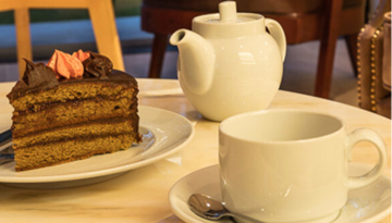 Coffee cup, teapot, and slice of chocolate cake on a table.