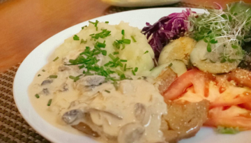 Plate with mashed potatoes, cream mushroom sauce, sliced tomato, cucumber, and greenery