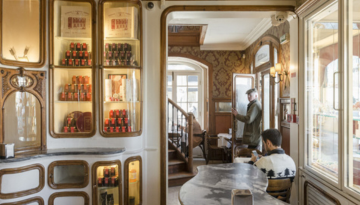 Cozy cafe interior with ornate decor and people seated at tables, reading or enjoying drinks.