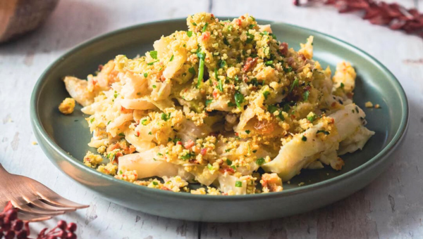 Plate of pasta topped with breadcrumbs and herbs on a gray table.