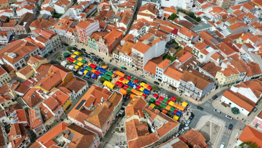 Aerial view of colorful market stalls among orange-roofed buildings in a small town.