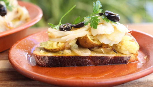 Open sandwich with shredded chicken, olives, and herbs on brown bread on a clay plate.