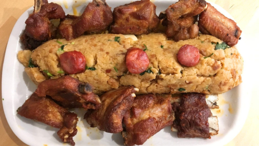 Dish with sausages and herbs surrounded by fried meat chunks on a white plate.