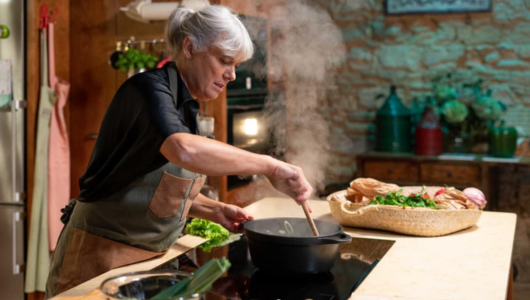 Person stirring a pot on a stove in a rustic kitchen with steam rising.