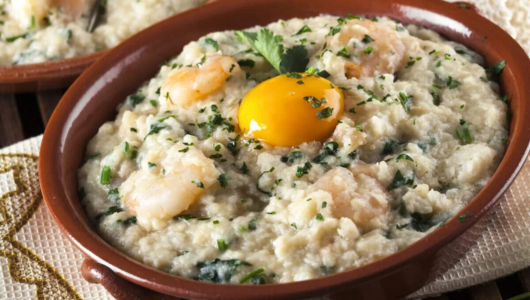 Shrimp and egg-topped creamy dish in a brown bowl with herbs.