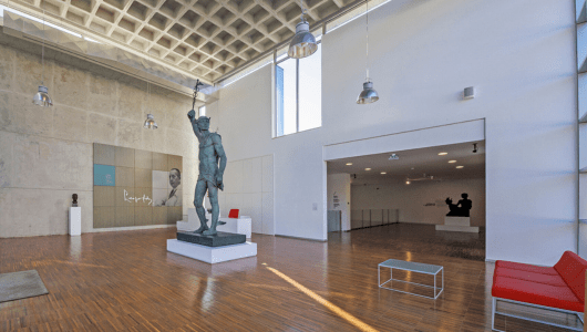 Spacious gallery with a central statue, red seating, and modern lighting.