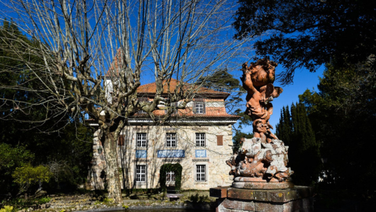 Stone building with red roof, bare trees, and sculpture in foreground on a sunny day.